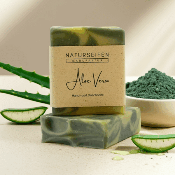 Zwei Stücke handgefertigte Aloe Vera Seife von Naturseifen Manufaktur, eine übereinander gestapelt. Die Seife ist grün marmoriert und hat eine naturfarbene Banderole mit der Aufschrift "Naturseifen Manufaktur Aloe Vera Hand- und Duschseife".