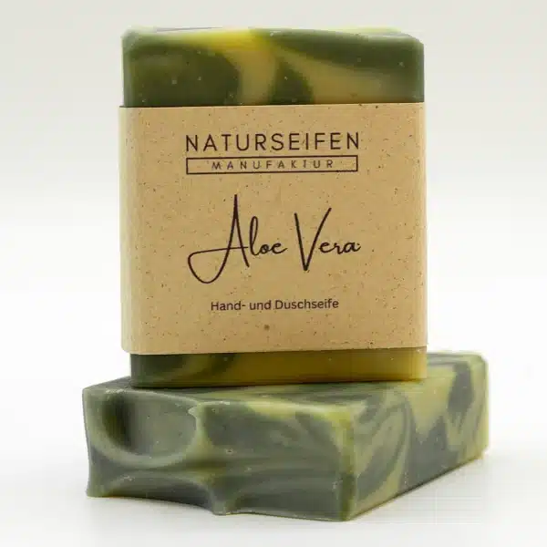 Zwei Stücke handgefertigte Aloe Vera Seife von Naturseifen Manufaktur, eine übereinander gestapelt. Die Seife ist grün marmoriert und hat eine naturfarbene Banderole mit der Aufschrift "Naturseifen Manufaktur Aloe Vera Hand- und Duschseife".