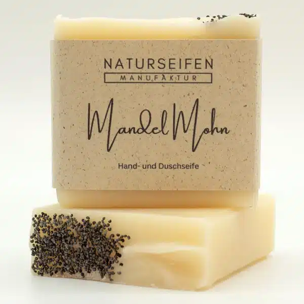 Zwei Stücke handgefertigte Mandel Mohn Seife von Naturseifen Manufaktur, eine übereinander gestapelt. Die Seife ist gelblich-beige mit Mohnsamen und hat eine naturfarbene Banderole mit der Aufschrift "Naturseifen Manufaktur Mandel Mohn Hand- und Duschseife".