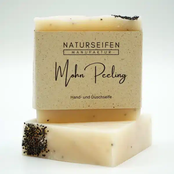 Ein Stück handgemachte Naturseife der Marke "Naturseifen Manufaktur" mit der Aufschrift "Mohn Peeling". Die Seife ist cremefarben mit kleinen schwarzen Mohnsamen und befindet sich auf einem weiteren Seifenstück derselben Sorte, vor einem neutralen Hintergrund.