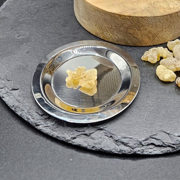 A silver incense plate with a piece of frankincense resin, placed on a slate base. Next to the plate are more pieces of frankincense.